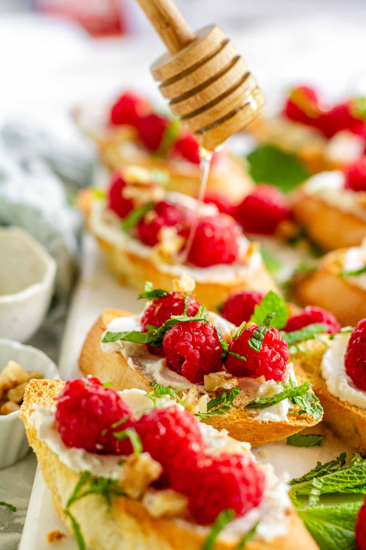 Toasted baguette slices topped with white spread, raspberries, chopped mint, walnuts, and honey.