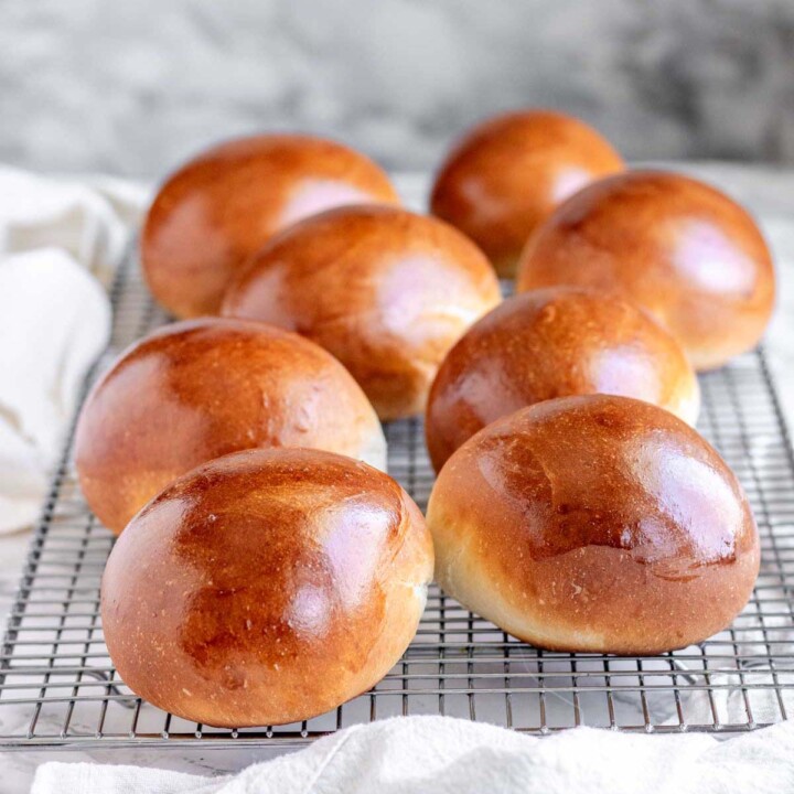 Golden brown homemade brioche buns cooling on a wire rack after baking.