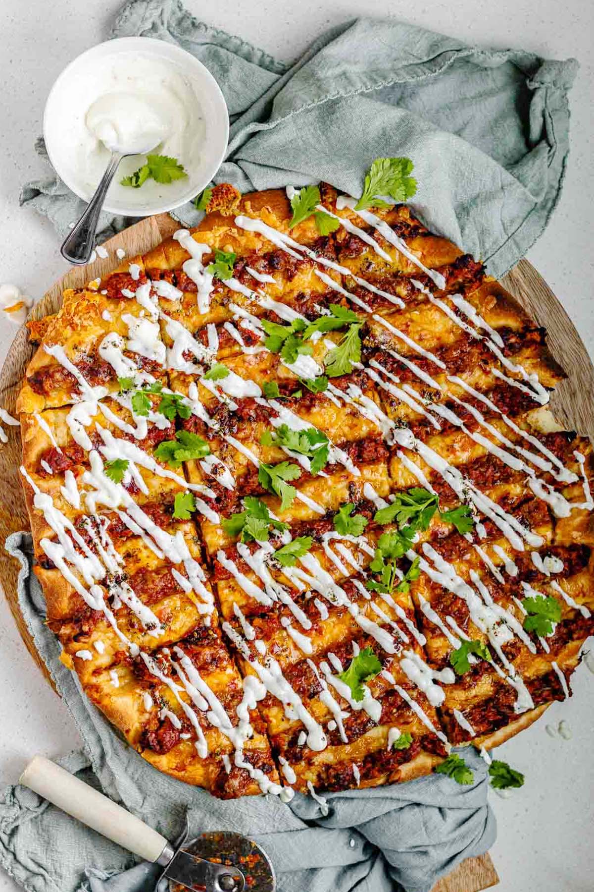Flatbread topped with lines of cooked meat and cheese, drizzled with yogurt sauce, and scattered with cilantro leaves.